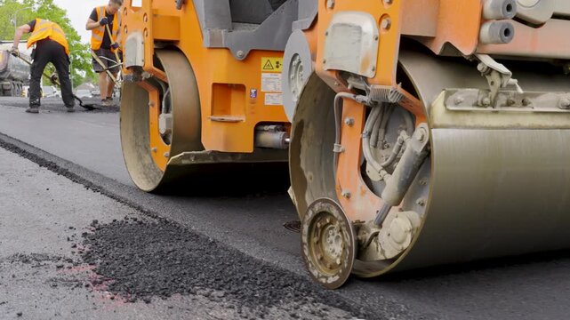 Heavy-duty road roller compacts fresh asphalt on a construction site, showcasing the machinery's powerful wheels and smooth surface