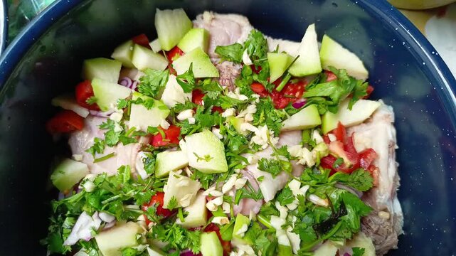 Raw chicken marinated with chopped vegetables in a blue enamel pot