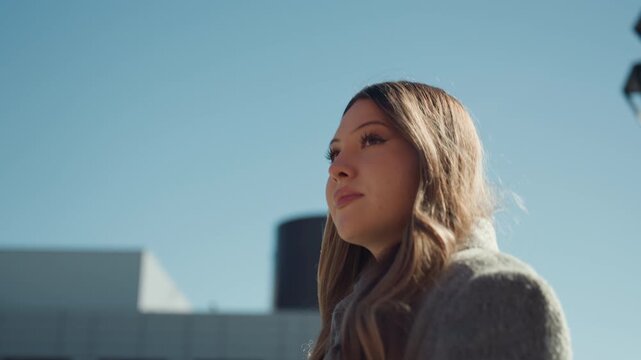 Pretty caucasian woman looking upward toward sky, confident entrepreneur posture, modern architecture backdrop, sunlight highlighting hair, serene expression, empowered mood, closeup composition