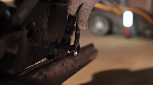 Mechanic's gloved hand using a socket wrench to tighten a bolt on a motorcycle engine during maintenance, close up showing precision, safety and professional repair care