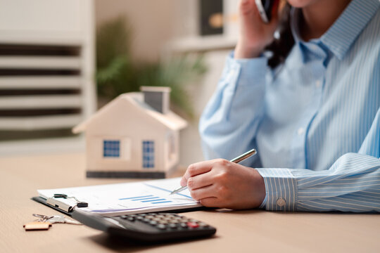 Real estate agent calling client for property contract and mortgage. Professional broker writing document with house model and calculator.
