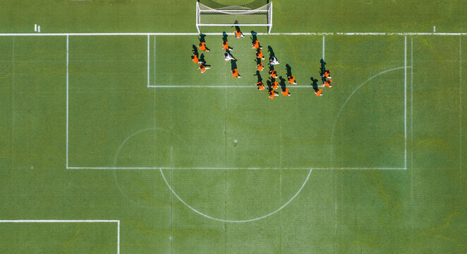 Aerial view of children in orange jerseys running across the soccer field during soccer practice at a sports park in Wuhan, China.