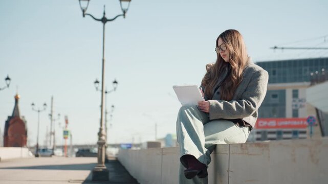 Pretty caucasian writer adjusting glasses outdoors, bench beside busy storefront, concentrated note taking on pad, wool coat, crisp sunlight, focused creative energy, modern urban backdrop