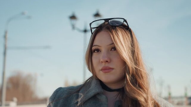 Stylish lady in winter coat outside. Fashionable woman standing under vintage lampposts during winter. Refined woman in wool coat and sunglasses on city boulevard during soft evening light