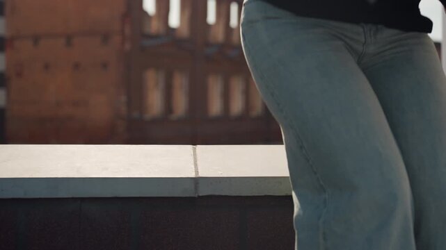 Pretty rooftop artist white woman sits, adjusts palette and prepares brush on ledge in denim, closeup of legs and hands, golden hour light on brick warehouse, intimate calm mood and thoughtful pause.