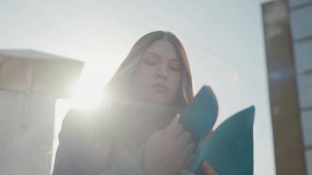 Reader with book. Young woman engrossed in novel outdoors. Literature enthusiast reviewing pages against sunrise backdrop. Serene scene of student immersed in reading with city skyline at dawn