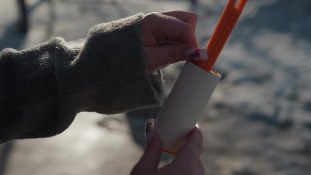 Closeup hands peeling lint roller outdoors, gray sweater sleeves, manicured nails delicately lift adhesive strip, tactile satisfying motion, winter sidewalk blurred background, intimate cozy routine