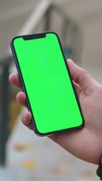 Hand with phone, Detailed view of person holding smartphone with green screen and seasonal outdoor surroundings