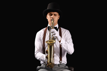 Fototapeta premium Male artist playing saxophone on black background