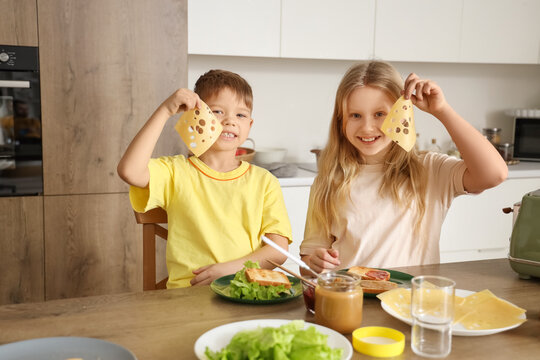 Little children with cheese and toasts at table in kitchen