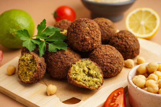 Wooden board with delicious falafel balls, tomatoes and chickpea on beige background, closeup