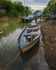 Obraz premium Blue Wooden Fishing Boat Anchored in a Muddy Canal.