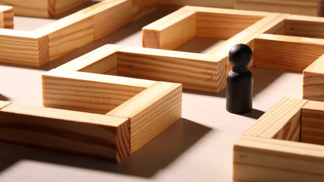 Woman taking human figure and moving black one in maze made of wooden blocks at table, closeup. Business strategy