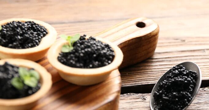 Tasty tartlets with black caviar on wooden table, closeup. Camera moving right