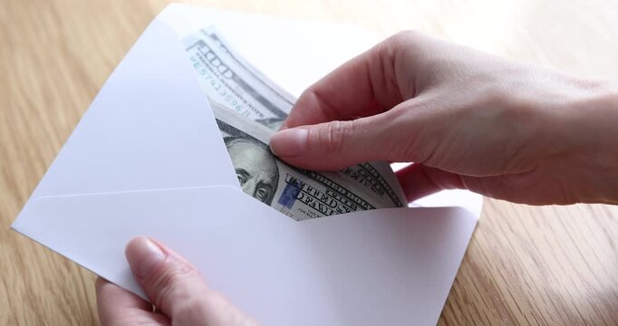 Woman opening envelope with dollar banknotes indoors, closeup
