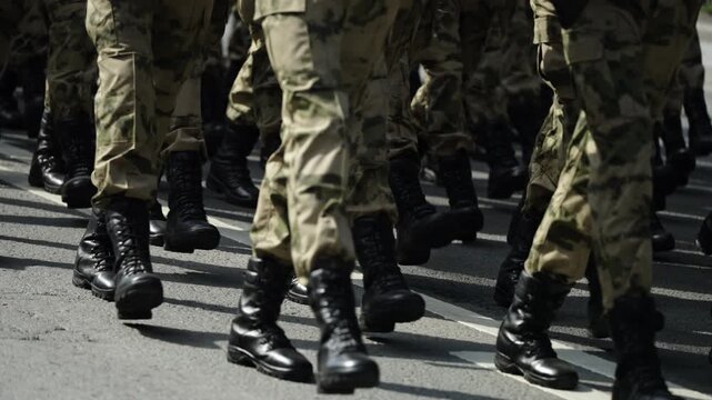 Close-up view of uniformed soldiers in camouflage marching in tight formation on a street, black combat boots striking asphalt in synchronized steps during a military parade