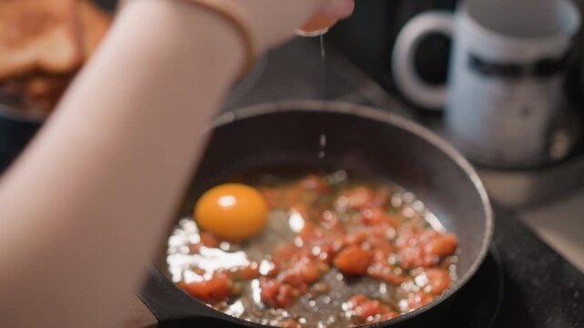 Egg breaks in pan. Cracked egg falls into oil skillet. Hands carefully split fresh egg into hot cooking mixture. Vivid yolk spills into sizzling oil as hands gently crack open fresh eggs
