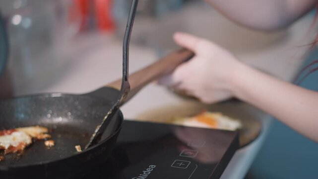 Frying egg in pan, stovetop spatula moves. Redhaired woman transfers crispy edged egg to plate, focused profile and steady hands, soft morning light, sizzling sound and warm kitchen atmosphere, simple