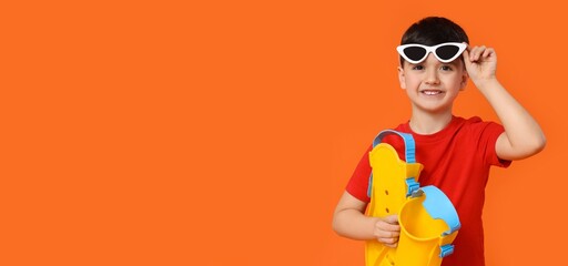 Cute little boy in sunglasses holding flippers on orange background with space for text © Pixel-Shot