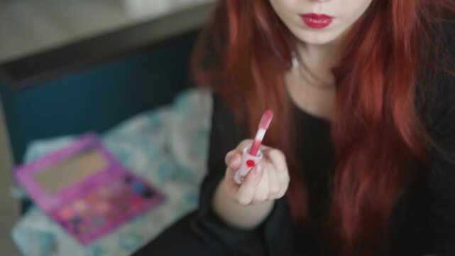 Redhaired woman applying lipstick gracefully. Female with fiery hair enhancing her lips charmingly. Woman with scarlet hair uses mirror light to perfect her lip makeup with playful intent