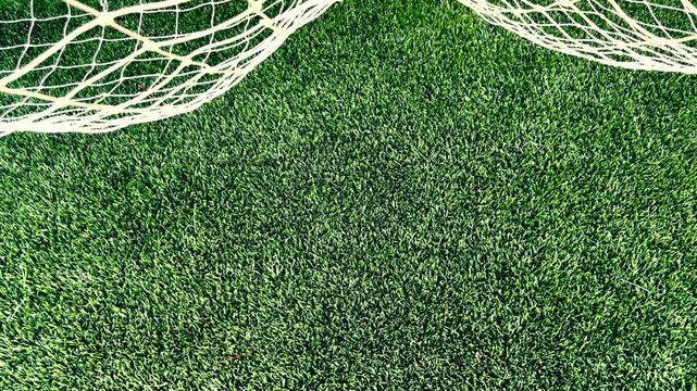 Top-down overhead view of a crisp white soccer goal net against a vibrant green artificial turf sports field, with smooth movement gliding left to right across the netting.