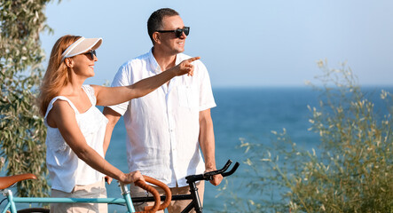 Mature couple with bicycles walking along sea shore on summer day © Pixel-Shot