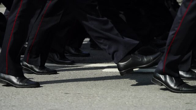 Close-up of uniformed marchers stepping in synchronized formation during a city street parade, showing polished black shoes and dark trousers in precise, disciplined cadence