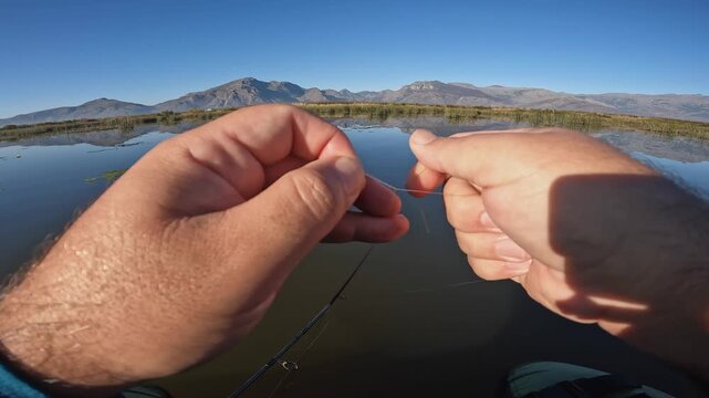 Angler ties fishing lure, hook on monofilament line, POV mountain lake