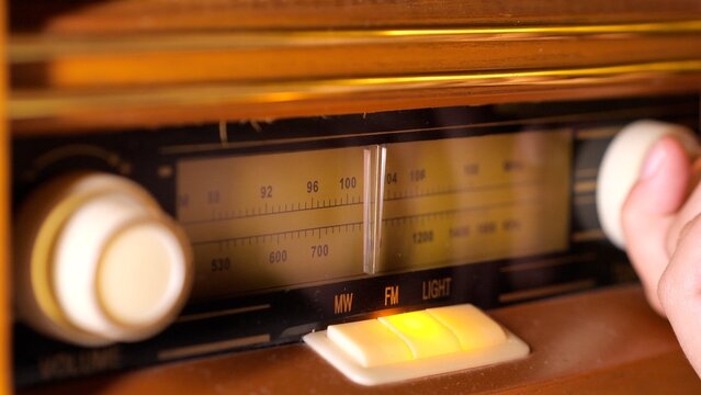 Hand adjusting the dial of an old wooden radio, searching for a specific frequency on the fm band, highlighting the nostalgic experience of traditional sound media