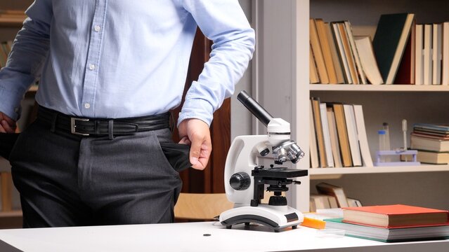 Researcher revealing empty pockets by a microscope and books, symbolizing a lack of funding and economic struggles in scientific research and education