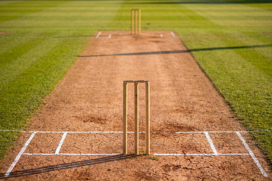 Cricket pitch photo with wooden stumps and crease lines on dry ground for sports background banner poster and match design