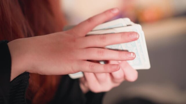 Closeup hands shuffling tarot deck, soft indoor light, reader fans cards with gentle gestures, visible red hair and manicured nails, cozy ritual mood, fortune foresight atmosphere
