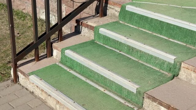 Worn green carpet on steps pickup entrance, frayed turf covering concrete stairs with white slip resistant strips, rusty metal