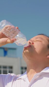 Vertical video, sweating profusely in the heat, a man gulps down a whole bottle of water at once.