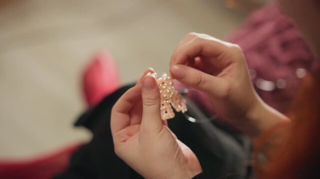 Precise jewelry making. Closeup of hands creating beaded bracelet with detailed focus. Skilled artisan meticulously threading beads to craft shimmering talisman bracelet in cozy lighting