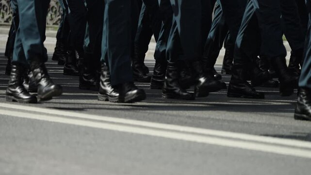 Close-up of uniformed personnel marching in precise formation along a roadway, black leather boots striking asphalt in synchronized steps convey discipline and ceremonial unity