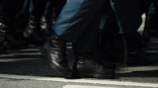 Close-up of uniformed marchers black leather boots striking the asphalt in synchronized formation along a street, followed by an empty roadway as the procession passes the frame
