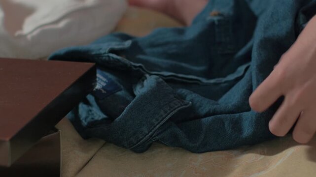 Close up of man hand holding a blue denim shirt on bed, lifestyle concept.