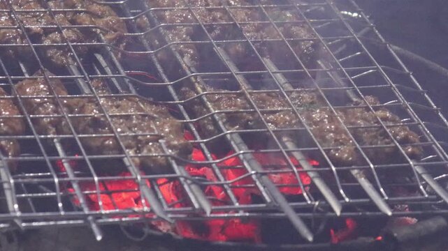 Kofta kebabs grilling over glowing charcoal with rising smoke
