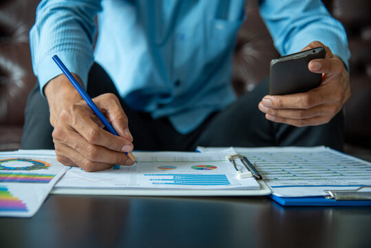 Asian Businessman reading financial spreadsheet graph chart Planning to analyze marketing data. Man reading financial graph chart Planning analyzing marketing data. Asian freelance writing paper
