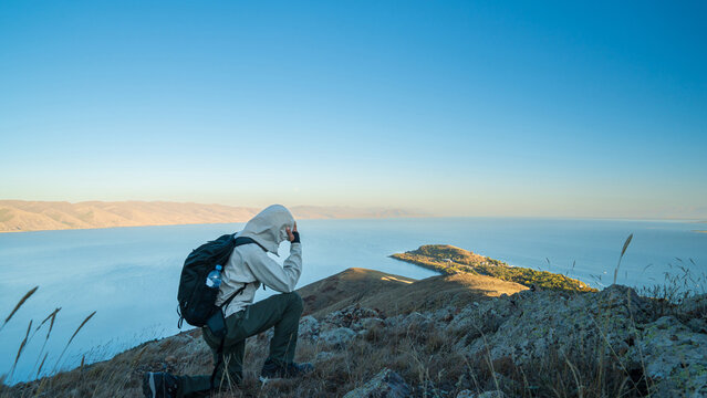 Traveler standing on a hill above Lake Sevan, Armenia, facing the vast landscape of water and mountains under a golden morning sky.