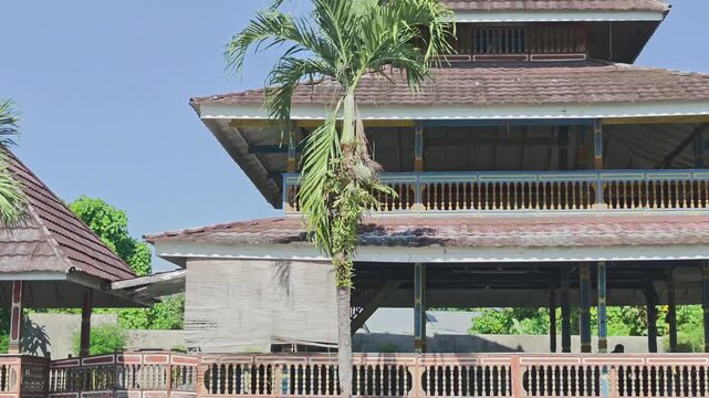 Slow motion panning shot from left to right capturing the authentic exterior of a traditional Indonesian wooden house. The footage showcases the classic multi-tiered roof, heritage pillars, wooden bal