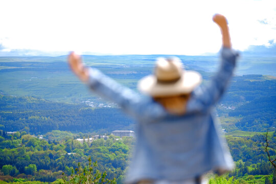 Out of focus back view of woman dreamer raising hands in front of valley scenery. Inspired traveler and explorer admiring beautiful panoramic green mountain peak.