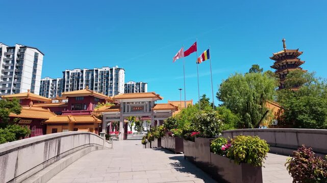 Flags flutter beside a traditional entrance with a pagoda nearby, set against modern skyscrapers in Shanghai. Ideal for projects highlighting cultural contrasts or urban development.