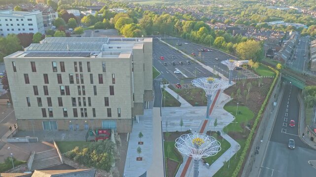 Digital Media Centre and surrounding urban landscape in Barnsley, South Yorkshire, England, during sunset with illuminated rose canopy installation and evening city atmosphere, aerial descent