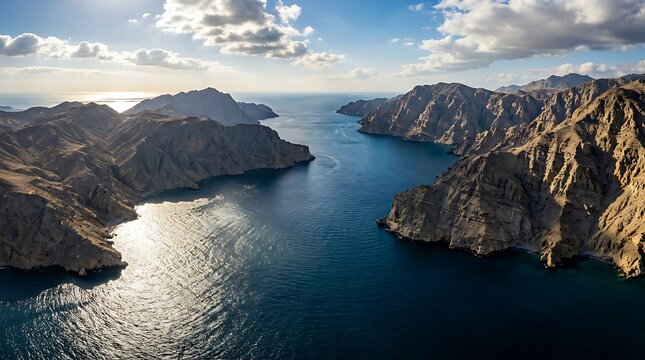 Aerial view of majestic rocky mountains surrounding the deep blue sea under a bright sunny sky with fluffy white clouds