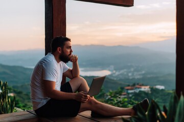 Obraz premium Man bearded working on laptop on balcony with mountain view at golden hour