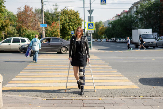 Young girl with a plastered foot in the orthosis and with crutches on a walk in the city
