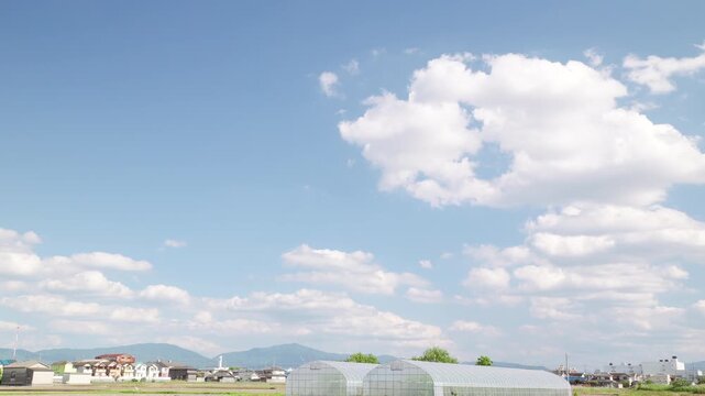 青空を白い雲が流れる田植えの頃の田園風景。早送り映像