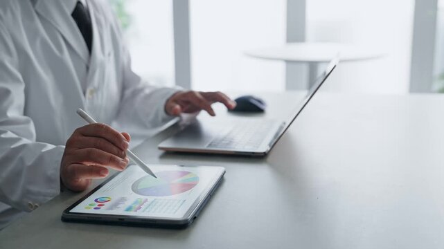 ノートパソコンとタブレットPCを使って作業する白衣の男性